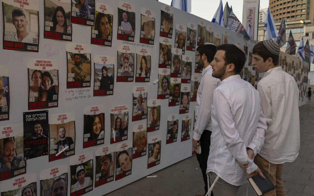 Des jeunes hommes regardant des photos d'Israéliens disparus et retenus en otage à Gaza, affichées sur un mur à Tel Aviv, le 20 octobre 2023. (Crédit : Petros Giannakouris/AP Photo)