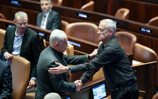 Le Premier ministre Benjamin Netanyahu serrant la main du ministre nouvellement nommé Benny Gantz lors d'une session plénière spéciale présentant le nouveau gouvernement d'urgence dans le plénum de la Knesset, à Jérusalem, le 12 octobre 2023. (Crédit : Noam Revkin Fenton/Flash90)