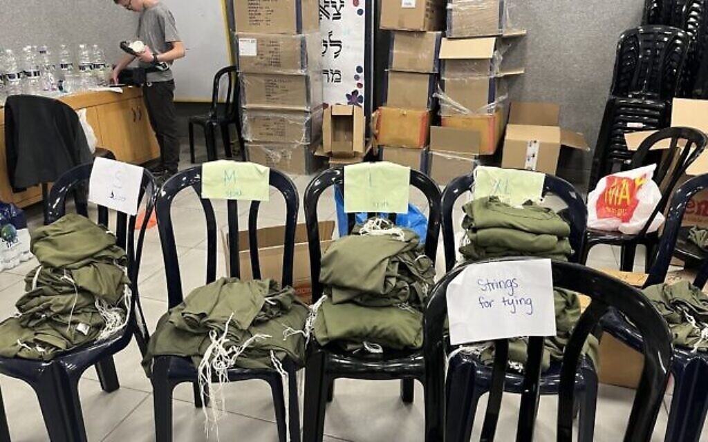 Des piles de vestes militaires et de cordes de tsitsit installées dans un hall d'école à Jérusalem, alors que des membres de la communauté préparent des tsitsit pour les soldats israéliens sur les lignes de front, le 19 octobre 2023. (Crédit : Shira Silkoff) 