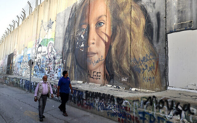 Des hommes passent devant une section de la barrière de sécurité d'Israël peinte d'un portrait de la détenue palestinienne Ahed Tamimi, le 6 novembre 2023 à Bethléem, en Cisjordanie. (Crédit : Hazem Bader / AFP)