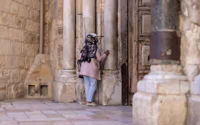 Une femme prie à l'entrée de l'église du Saint-Sépulcre dans la vieille ville de Jérusalem, le 21 novembre 2023. (Crédit : Kenzo TRIBOUILLARD / AFP)