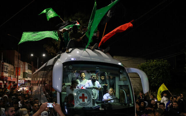 Un bus transportant du personnel de la Croix-Rouge et des prisonniers palestiniens libérés des prisons israéliennes en échange d'otages innocents libérés par le Hamas, traverse une foule de partisans brandissant des drapeaux palestiniens et du Hamas à Ramallah, en Cisjordanie, tôt le 26 novembre 2023. (Crédit : AHMAD GHARABLI / AFP)