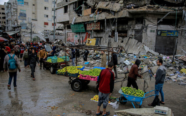 Des Palestiniens vendant des légumes devant un bâtiment détruit, à Gaza City, le 27 novembre 2023. (Crédit : Omar El-Qattaa/AFP)