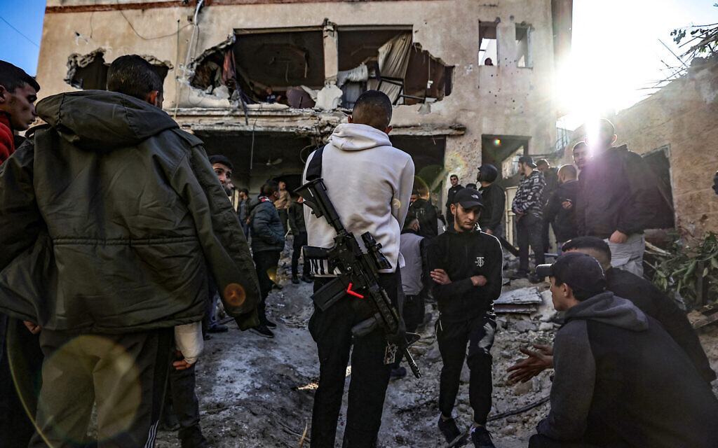 Un Palestinien armé se tenant parmi des habitants de Jénine alors qu'ils examinent les dommages subis par une maison lors d'un raid de Tsahal dans la région, le 29 novembre 2023. (Crédit : Zaïn Jaafar/AFP)