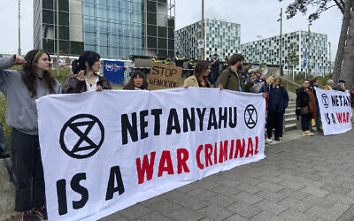 Des militants brandissant une bannière dénonçant le Premier ministre Benjamin Netanyahu pour les actions d'Israël pendant la guerre contre le Hamas, à l'entrée de la Cour pénale internationale, à La Haye, aux Pays-Bas, le 23 octobre 2023. (Crédit : Aleks Furtula/AP)