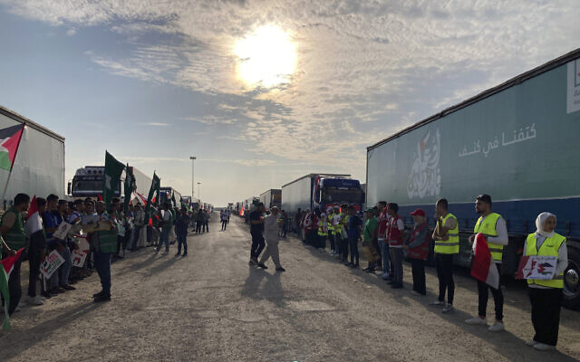Des bénévoles se tenant devant des camions transportant de l'aide humanitaire aux Palestiniens au poste-frontière de Rafah, en Égypte, le 31 octobre 2023. (Crédit : Ahmed Hatem/AP)
