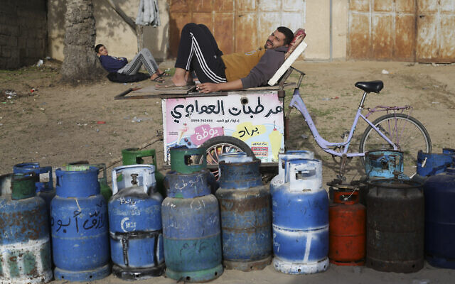 Un homme est assis avec des bidons vides en attendant qu'ils soient remplis du gaz domestique d'un réservoir qui est entré dans l'enclave palestinienne via le point de passage de Rafah avec l'Égypte, à Rafah dans le sud de la bande de Gaza le 25 novembre 2023. (Crédit : AP Photo/Hatem Ali)