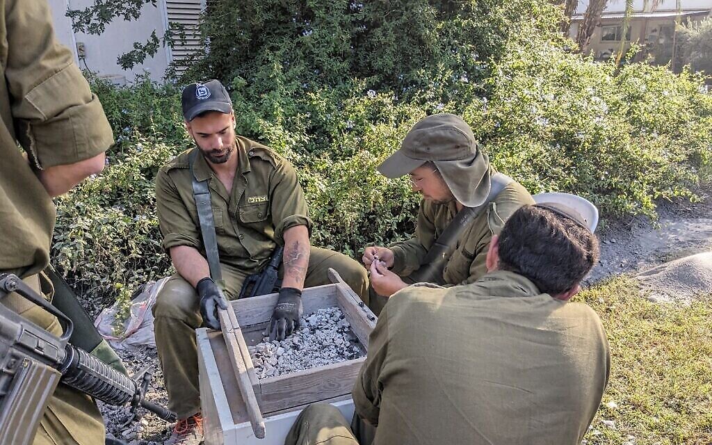 Des soldats aident les archéologues à passer au crible les restes d'une maison du kibboutz Nir Oz, le 9 novembre 2023. (Crédit : Melanie Lidman/Times of Israël)
