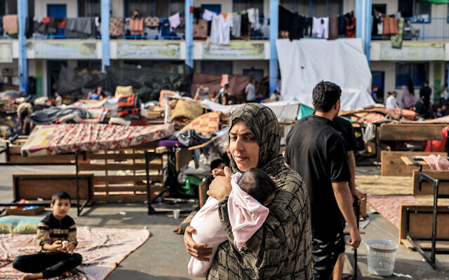 Une femme porte un nourrisson dans la cour de récréation d'une école contrôlée par l'Office de secours et de travaux des Nations unies pour les réfugiés de Palestine (UNRWA) qui a été convertie en abri pour les Palestiniens déplacés, à Khan Yunis dans le sud de la bande de Gaza, le 25 octobre 2023. (Crédit : Mahmud Hams/AFP)