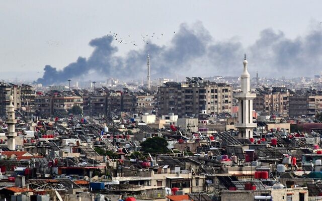 Des volutes de fumée s'élèvent au-dessus des bâtiments après une frappe israélienne dans la banlieue de Damas, le 22 novembre 2023. (Crédit : AFP)