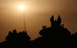 Des troupes israéliennes se tenant sur le dessus de chars et de véhicules militaires au coucher du soleil, après la reprise des batailles entre Israël et le Hamas, près de la frontière avec la bande de Gaza, le 2 décembre 2023. (Crédit : Jack Guez/AFP)