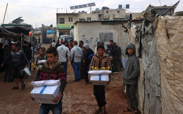 Des Syriens déplacés transportent des cartons de secours du Programme alimentaire mondial (PAM) des Nations unies avant la fin de l'acheminement de l'aide, dans le camp d'Atma, à la périphérie d'Idlib, dans le nord-ouest de la Syrie aux mains des rebelles, le 6 décembre 2023. (Crédit : AAREF WATAD / AFP)