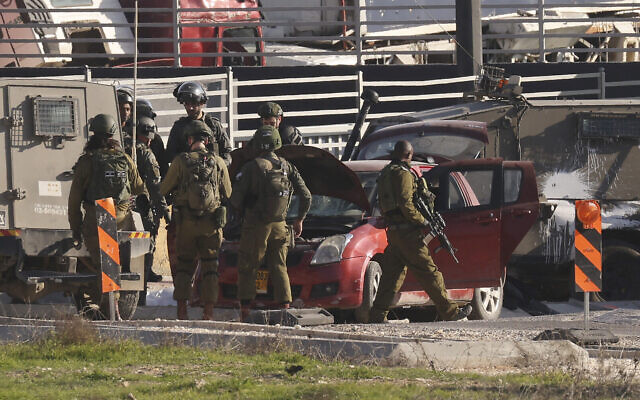 Les forces de sécurité israéliennes encerclent une voiture utilisée par un Palestinien pour percuter des soldats israéliens à l'entrée du camp de réfugiés d'al-Fawwar, au sud d'Hébron en Cisjordanie, le 30 décembre 2023. (Crédit : Hazem Bader/AFP)
