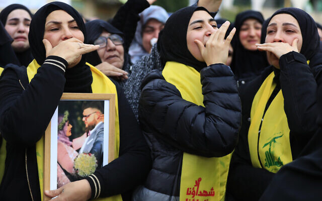 Des personnes en deuil, enveloppées dans des drapeaux du Hezbollah, assistant à la procession funéraire d'un terroriste du Hezbollah et de deux autres civils tués par une frappe aérienne israélienne qui aurait touché leur maison la veille au soir, à Bint Jbeil, au Sud-Liban, le 27 décembre 2023. (Crédit : Mohammed Zaatari/AP Photo)