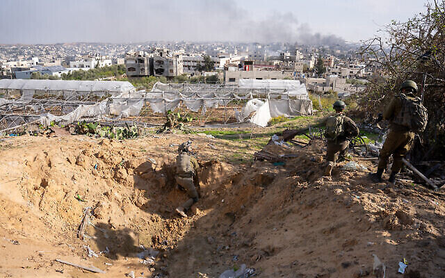 Des troupes israéliennes se tiennent près d'un cratère creusé par une frappe aérienne, alors que de la fumée s'élève de Jabaliya, dans le nord de la bande de Gaza, le 7 décembre 2023. (Crédit : Emanuel Fabian/Times of Israël)