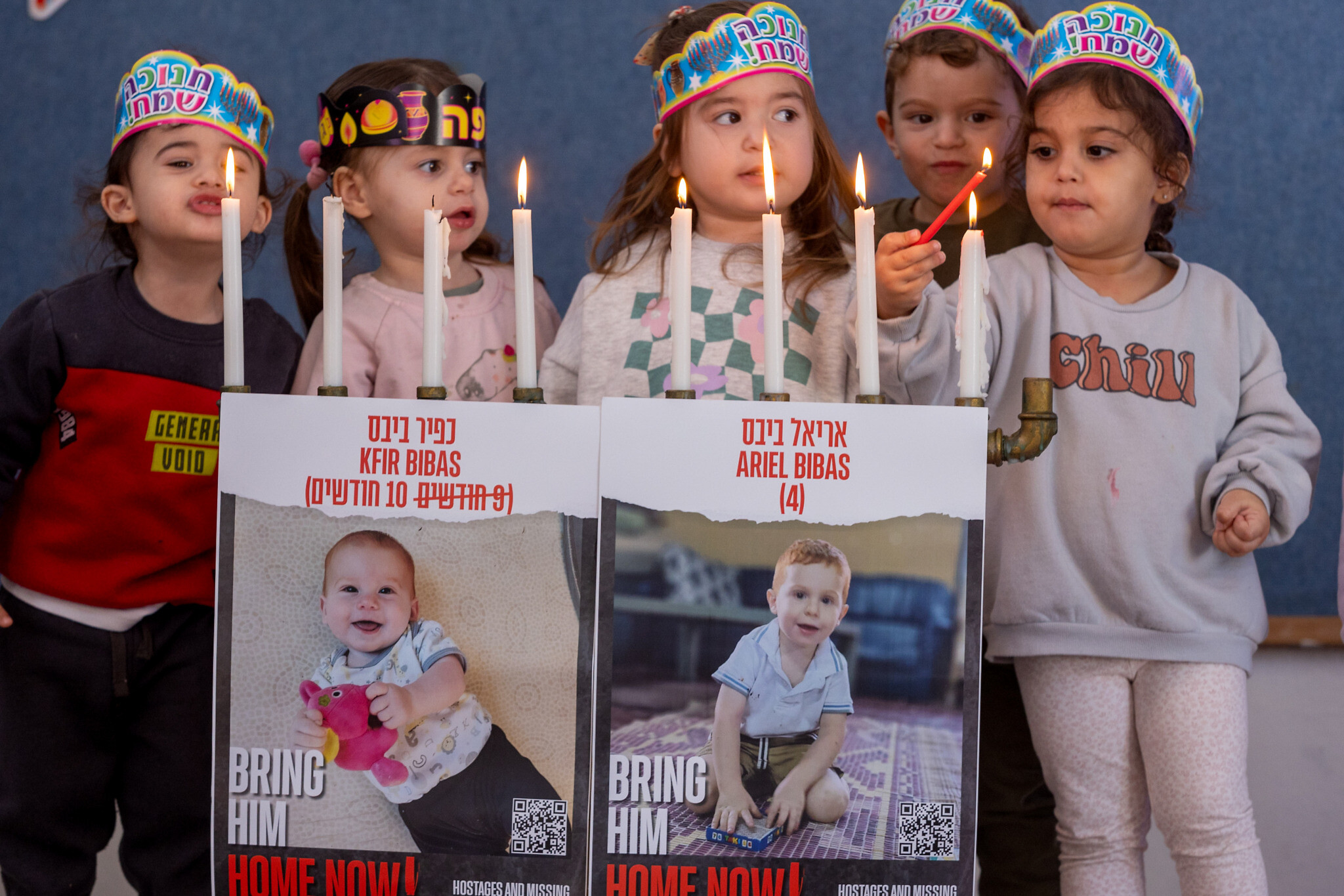 Des photographies de Kfir et Ariel Bibas, retenus en otage par les terroristes du Hamas, sur une menorah allumée par des enfants dans une crèche du Moshav Yashresh, dans le centre d'Israël, pendant Hanoukka, le 12 décembre 2023. (Crédit :  Yossi Aloni/Flash90)