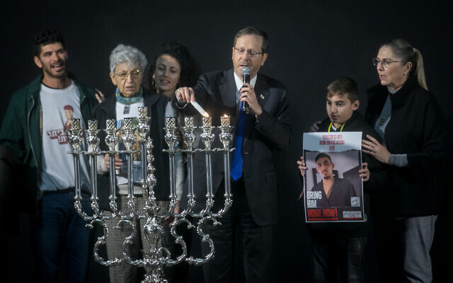 Le président Isaac Herzog et Michal Herzog allument des bougies pour Hanoukka avec Dvora Leshem, grand-mère de Romi Goren, otage, et d'autres membres des familles de captifs sur la place des Otages de Tel Aviv, le 13 décembre 2023. (Crédit : Miriam Alster/Flash90)