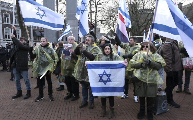Des manifestants brandissqnt des drapeaux israéliens et néerlandais, et tenant des photos des otages enlevés lors de l'attaque transfrontalière du Hamas en Israël le 7 octobre, lors d'une manifestation devant la Cour internationale de justice, à La Haye, aux Pays-Bas, le 11 janvier 2024 (Crédit : Patrick Post/AP)