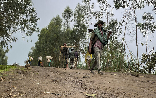 Un combattant armé non identifié, alors que des villageois fuient avec leurs biens dans l'autre direction, près du village de Chenna Teklehaymanot, dans la région d'Amhara, dans le nord de l'Éthiopie, le 9 septembre 2021. (Crédit : AP)