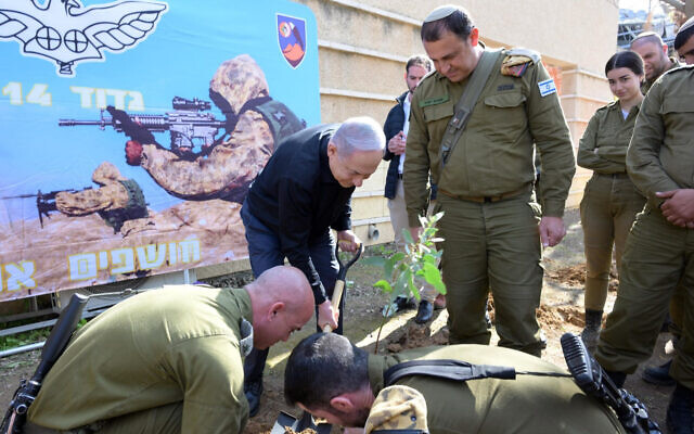 Le Premier ministre Benjamin Netanyahu, en noir, plantant un arbre sur une base militaire près de Gaza, le 25 janvier 2024. (Crédit : Amos Ben Gershom/GPO)