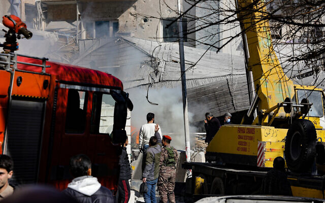 Les forces de sécurité et des badauds rassemblés devant un bâtiment détruit dans une frappe attribuée à Israël, à Damas, le 20 janvier 2024. (Crédit : Louai Beshara/AFP)