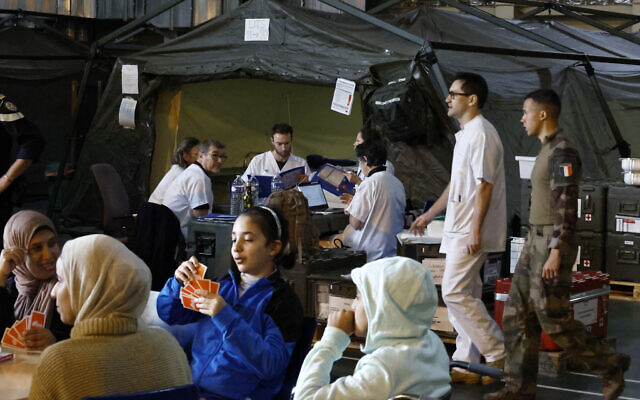 Des Palestiniens jouant aux cartes devant le personnel soignant militaire à bord du navire militaire français LHD Dixmude, qui sert d'hôpital pour soigner les Palestiniens blessés, dans le port égyptien d'al-Arish, le 21 janvier 2024. (Crédit : Khaled Desouki/AFP)