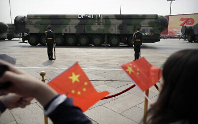 Des spectateurs agitant des drapeaux chinois alors que des véhicules militaires transportant des missiles balistiques nucléaires DF-41 roulent lors d'un défilé pour commémorer le 70e anniversaire de la fondation de la Chine communiste, à Pékin, le 1er octobre 2019. (Crédit : Mark Schiefelbein/AP/ Dossier)