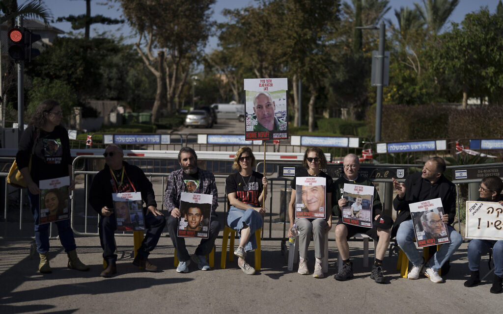 Carmit Palty Katzir tenant un poster de son frère Elad alors que des parents et des amis d'otages sont assis dans une rue devant la résidence privée du Premier ministre Benjamin Netanyahu, à Césarée, le 20 janvier 2024. (Crédit : Leo Correa/AP Photo)