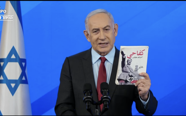 Le Premier ministre Benjamin Netanyahu brandissant un exemplaire de "Mein Kampf" d'Adolf Hitler en arabe, récupéré à Gaza, lors d'une conférence de presse sur la guerre en cours contre le Hamas, le 27 janvier 2024. (Crédit : Capture d'écran)