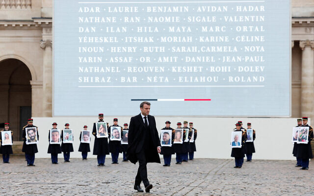 Le président français Emmanuel Macron marche devant des membres de la Garde républicaine française tenant des portraits des 42 citoyens français et franco-israéliens tués, lors d'une cérémonie d'hommage aux victimes françaises de l'attaque du Hamas contre Israël le 7 octobre, au complexe commémoratif des Invalides à Paris, le 7 février 2024. (Crédit : GONZALO FUENTES / POOL / AFP)