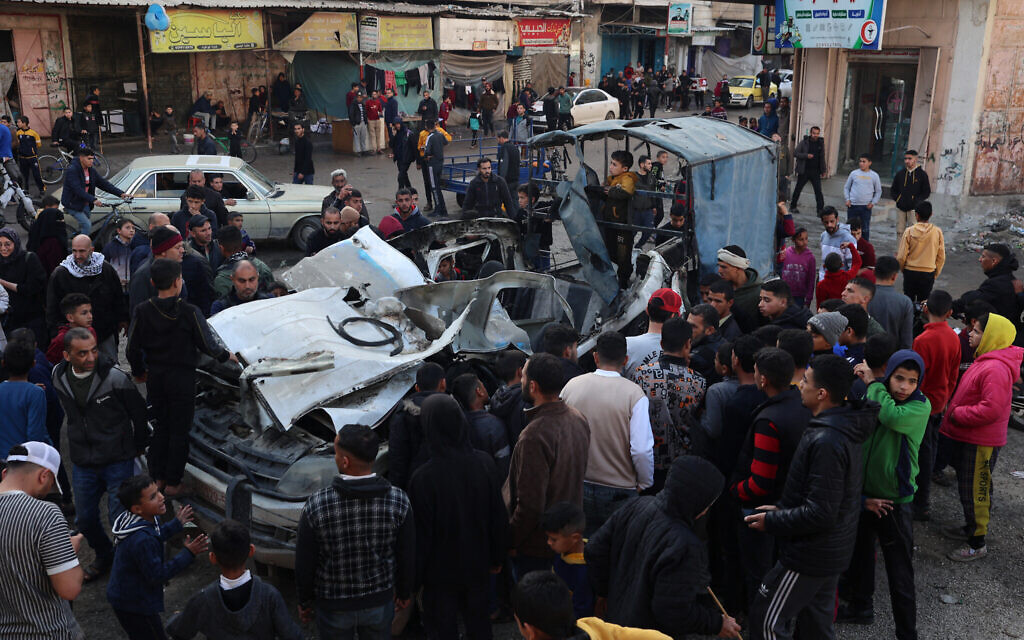 Des Gazaouis autour de la carcasse d'une voiture de police palestinienne qui aurait été détruite dans un bombardement israélien à Rafah, dans le sud de la bande de Gaza, le 10 février 2024. (Crédit : SAID KHATIB / AFP)