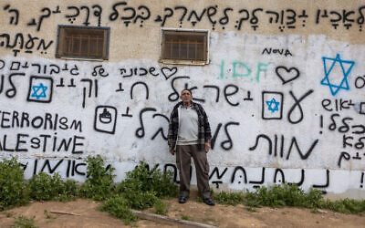 Shuki Yossef, 63 ans, pose à côté d'un graffiti en hébreu et en anglais portant des slogans contre l'attaque du 7 octobre par des combattants du Hamas, à Ofakim, une ville du sud d'Israël, à environ 25 kilomètres de la bande de Gaza, le 6 février 2024. (Crédit : Menahem Kahana / AFP)