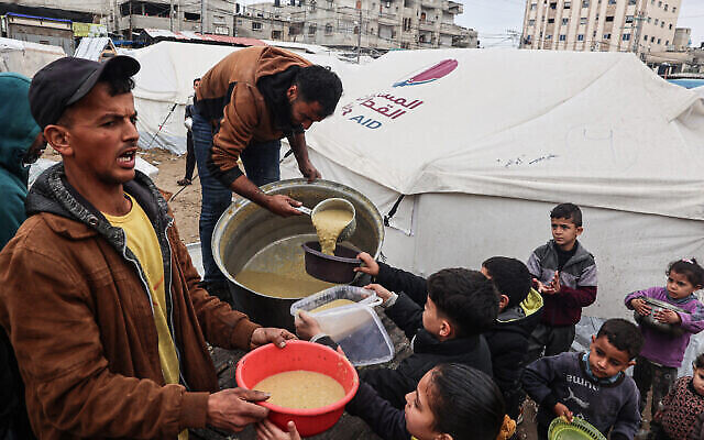 Des bénévoles distribuent des rations de soupe de lentilles corail à des Palestiniens déplacés à Rafah, dans le sud de la bande de Gaza, le 18 février 2024 (Crédit : SAID Khatib/AFP)