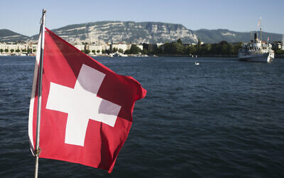 Le drapeau national suisse devant le lac Léman, à Genève, le 13 juin 2021. (Crédit : Markus Schreiber/AP)