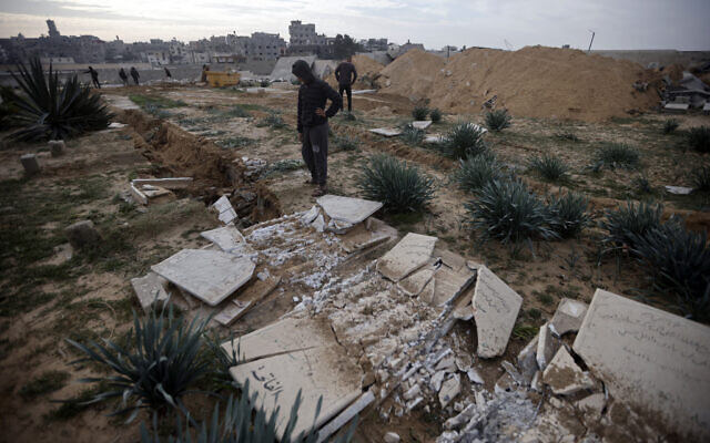 Des Palestiniens inspectent des tombes endommagées suite à un raid israélien dans un cimetière du camp de Khan Younès dans le sud de la bande de Gaza, le 17 janvier 2024. (Crédit : AP Photo/Mohammed Dahman)