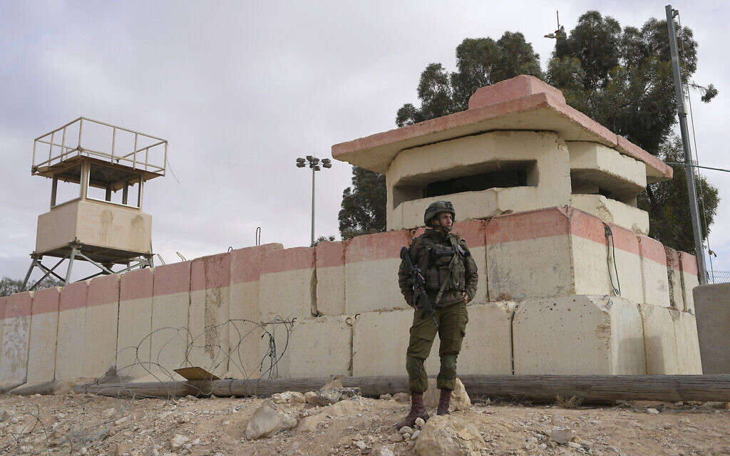 Un soldat israélien regarde des manifestants bloquer les aides humanitaires à destination de la bande de Gaza au poste-frontière de Nitzana, avec l'Égypte, dans le sud d'Israël, le 2 février 2024. (Crédit :  AP Photo/Tsafrir Abayov)