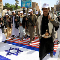 Des membres des Houthis soutenus par l'Iran au Yémen marchent sur des drapeaux israéliens et américains peints dans la rue à Sanaa lors d'un rassemblement de soutien aux Palestiniens dans le cadre de la guerre entre Israël et le groupe terroriste Hamas à Gaza, le 28 février 2024. (Crédit : Mohammed Huwais/AFP)
