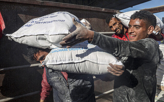 Des travailleurs déchargeant des sacs d'aide humanitaire entrés à Gaza par camion à travers le poste-fronière israélien de Kerem Shalom, , à Rafah, dans le sud de la bande de Gaza, le 17 février 2024. (Crédit : Saïd Khatib/AFP)