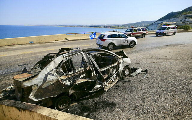 Une patrouille de la FINUL (Force intérimaire des Nations unies au Liban) passe devant une carcasse de voiture prise pour cible dans une frappe israélienne près de Naqoura, dans le sud du pays, le 2 mars 2024. (Crédit : AFP)