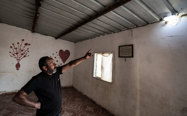 Mohamad Hassouna montrant un trou dans le toit d'un bâtiment causé par un projectile qui a blessé sa fille de 7 ans, Amina, dans leur village bédouin, non reconnu par les autorités israéliennes, dans le sud du désert du Néguev, le 14 avril 2024. (Crédit : Ahmad Gharabli/AFP)