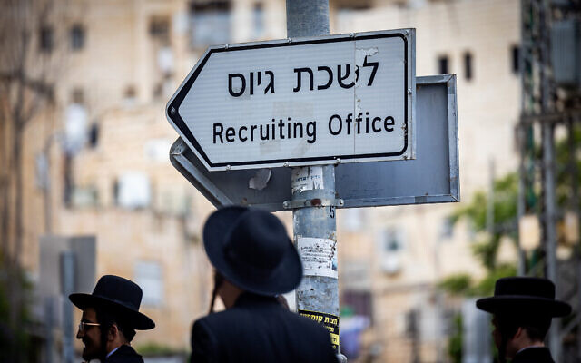 Des Juifs ultra-orthodoxes près d'un panneau indiquant "bureau de recrutement de l'armée" lors d'une manifestation contre l'enrôlement des haredim dans l'armée, à Jérusalem, le 1er mai 2024. (Crédit : Yonatan Sindel/Flash90)