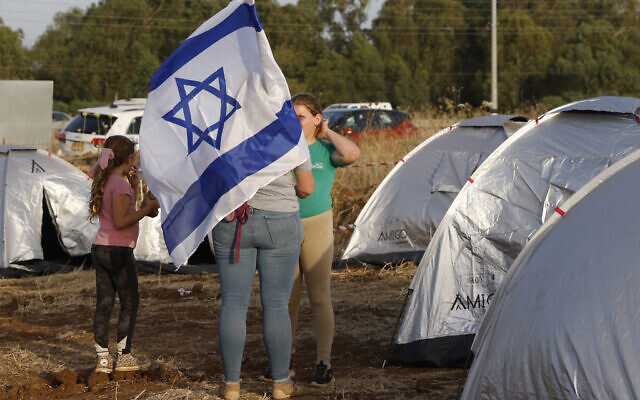Des Israéliens évacués des communautés du nord près de la frontière libanaise en raison des tensions transfrontalières actuelles, se tiennent au milieu de tentes avec un drapeau national lors d'un rassemblement près d'Amiad, exigeant de retourner dans leurs maisons, 23 mai 2024. (Crédit : Jalaa Marey/AFP)