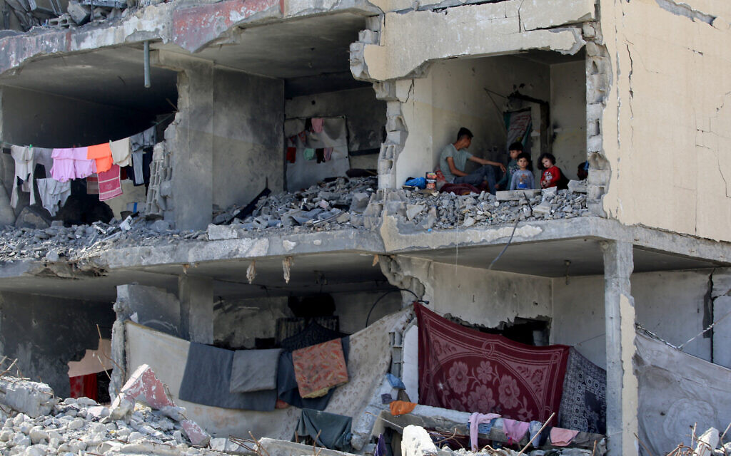 Un Palestinien et ses enfants assis dans une pièce détruite d'un bâtiment lourdement endommagé, par une frappe aérienne imputée à Israël, à Rafah, dans le sud de la bande de Gaza, le 22 mai 2024. (Crédit : Eyad al-Baba/AFP)