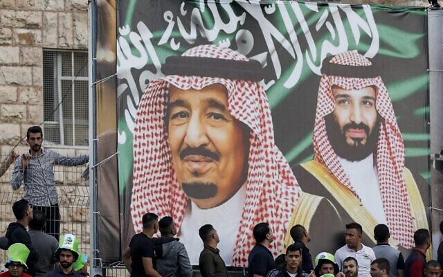 Des supporters de football devant une grande bannière représentant le roi d'Arabie saoudite Salman bin Abdulaziz, au centre, et le prince héritier Mohammed bin Salman, à droite, lors d'un match de qualification de la région Asie en vue de la Coupe du monde opposant la Palestine et l'Arabie saoudite dans la ville d'al-Ram, en Cisjordanie, le 15 octobre 2019. (Crédit : Ahmad GHARABLI / AFP / File)