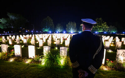 Un officier britannique regardant des tombes illuminées, dans le cadre des commémorations du 80e anniversaire du débarquement des Alliés en Normandie pendant la Seconde Guerre mondiale, au cimetière militaire de Bayeux, à Bayeux, dans le nord-ouest de la France, le 5 juin 2024. (Crédit : Loïc Venance/AFP)