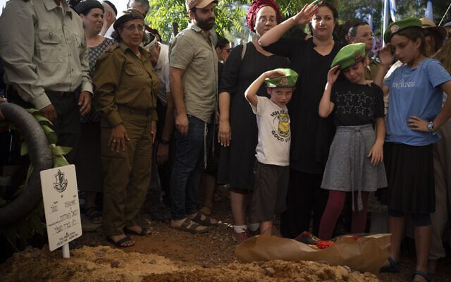 La femme et les enfants du sergent-chef Rafael Kauders, réserviste de Tsahal, qui a été tué lors d'une attaque de drone du Hezbollah sur le nord d'Israël le 5 juin, saluent lors de ses funérailles dans un cimetière de l'implantation de Kfar Etzion en Cisjordanie, le 6 juin 2024. (Crédit : AP Photo/Leo Correa)