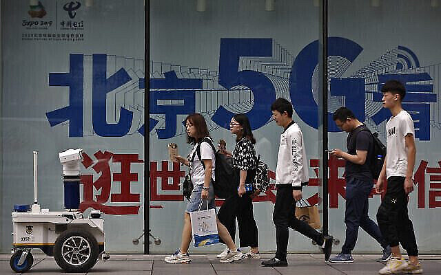 Photo d'illustration : Un robot de la police avec des caméras de surveillance filme des gens passant devant une publicité pour la 5G dans un quartier commercial de Pékin, le 15 mai 2019 (Crédit : AP/Andy Wong)