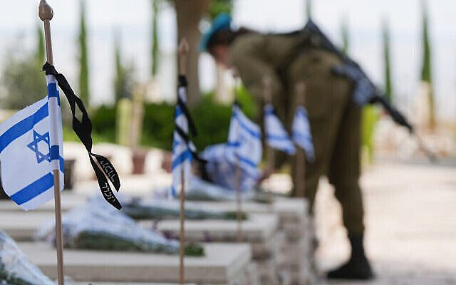 Un soldat de Tsahal dépose des fleurs et des drapeaux sur les tombes des soldats tombés au combat au cimetière militaire de Kiryat Shmona, le 12 mai 2024, à l'approche de Yom HaZikaron. (Crédit : Ayal Margolin/Flash90)
