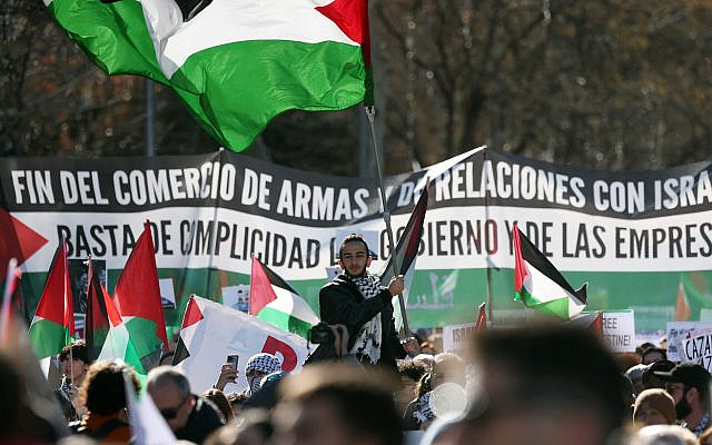 Un homme brandit un drapeau palestinien devant une banderole demandant l'arrêt de la livraison d'armes à Israël et dénoncant la complicité du gouvernement, pendant une manifestation à Madrid, le 20 janvier 2024. (Crédit : by Pierre-Philippe MARCOU / AFP)