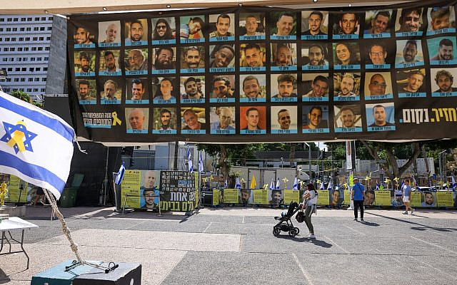 Des passants devant des affiches des otages détenus par des terroristes palestiniens à Gaza, sur la Place des Otages, à Tel Aviv, le 10 octobre 2025. (Crédit : Ahmad Gharabli/AFP)